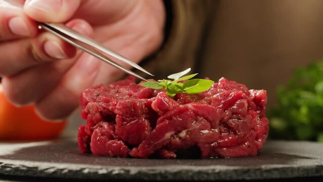 Chef cooking Raw beef meat tartar with sauce, man cutting steak tartare, making delicious french dish in modern restaurant. Fresh eco angus meat. 