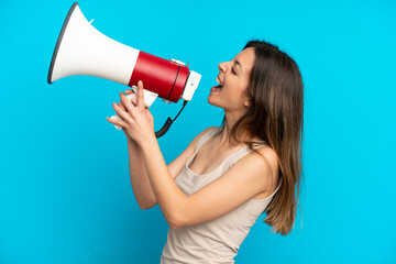 Young caucasian woman isolated on blue background shouting through a megaphone to announce...