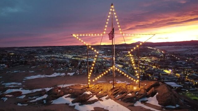 A lighted holiday star atop Castle Rock, in Castle Rock, Colorado.  Drone shot at sunset in the Colorado mountains.
