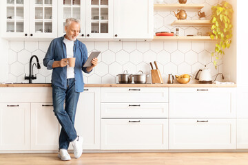 Smiling Senior Man With Digital Tablet And Coffee Relaxing In Kitchen