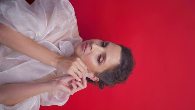 vertical portrait of a woman in a jumper on a red background at Christmas wearing earrings