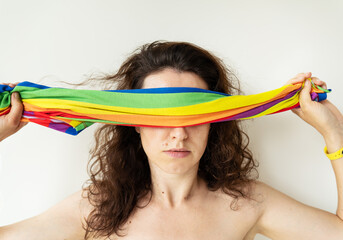 A girl covers her eyes with a bright multi-colored rainbow LGBT flag. LGBT girl. There is no...