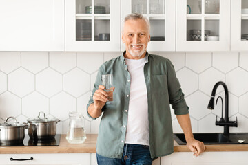 Smiling Senior Man With Glass Of Water In Hand Posing In Kitchen