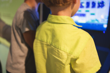 Kids play slot machine at amusement theme park, children play arcade gaming machine, racing and shooting game at the fair, teenagers having fun playing simulator video games