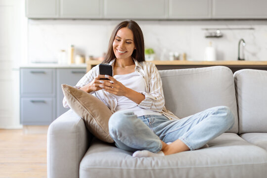 Happy Young Woman Messaging On Smartphone While Relaxing On Couch At Home
