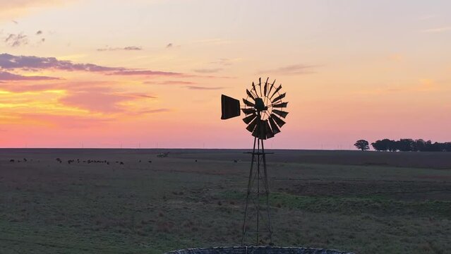 Slow left to right circle shot of a turning windmill at sunset in South Africa. The shot reveals glorious colours in the sunset sky