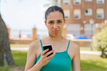 Young pretty woman using mobile phone at outdoors with sad expression