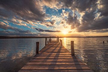 Small old fishing Dock at the lake and scenic sunset with dramatic cloudscape over sea - obrazy, fototapety, plakaty