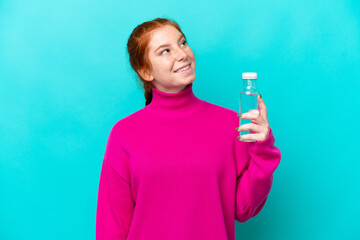 Young caucasian reddish woman with a bottle of water isolated on blue background looking up while...