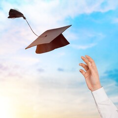 The student's hand hold a graduation cap on sky background