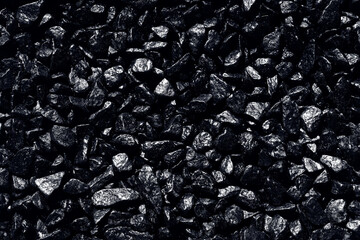 Black background. Black pebbles of irregular shape, evenly poured onto the surface. Monochrome photo.