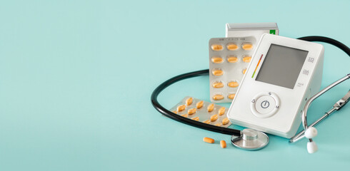 Electronic medical tonometer with high blood pressure pills on a blue background with copy space