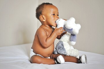 Childcare Concept. Portrait of cute little African  baby wearing bodysuit lying on white bedsheets...