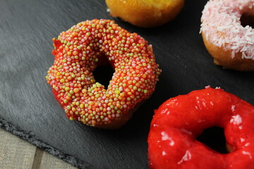A red glazed doughnut with sprinkles lies on a black tray. Donut Sweets Day National Food