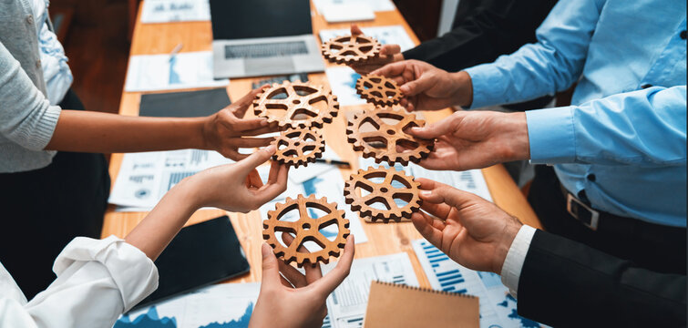 Group of multiracial business people joining gear wheels together over table as effective unity and productive teamwork concept. Efficient system business team process for solution solving. Meticulous