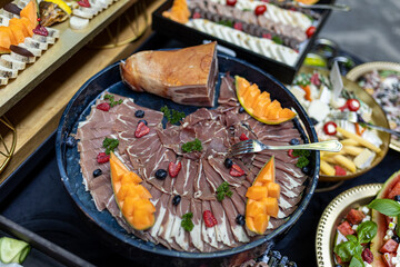 Fototapeta premium Cold meat delicatessen snacks, Italian prosciutto on round black dish on table of restaurant. 