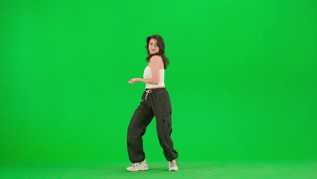 Attractive woman in white top dancing energetic jazz funk moves on chroma key green screen background in a studio.