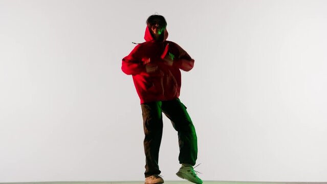 Attractive woman in red hoodie dancing jazz funk dance elements, isolated on white background green neon light.