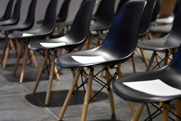 Rows of empty black chairs with white papers in the conference hall. Selective focus. Low DOF
