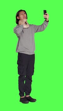 Side view of guy having cervical neck brace makes phone call informing family about his vertebral fracture injury. Full body greenscreen of wounded man wearing medical foam collar, speaking on