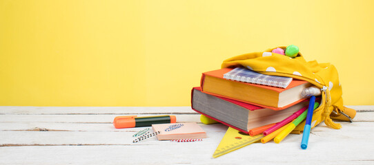 Yellow backpack with white polka dots with different colorful stationery on table. Yellow background. Back to school. Banner design.