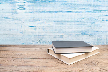 Composition with hardback books, fanned pages on wooden deck table and blue background. Books...