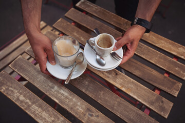 Waiter removing dirty dishes from the tables in cafe. Dirty used empty espresso coffee cappuccino cups close up. Empty cups of coffee on wooden table. Service concept. Waiter working in open terrace.