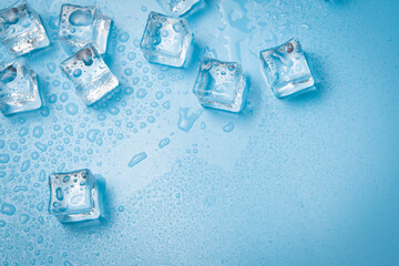 Ice cubes with water drops scattered on a blue background, top view