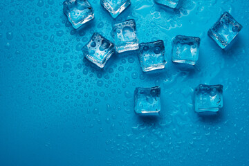 Ice cubes with water drops scattered on a blue background, top view