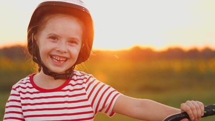 Young girl helmet-clad stands with laughter warming heart with sunset in field