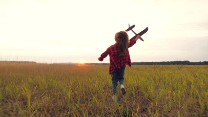 Girl runs with toy airplane in hand across grass field in direction of sunset