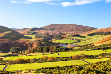 Expansive views of a valley in Scottish Highlands in colourful autumn colours with a lake and a small farm with sheep on a sunny day
