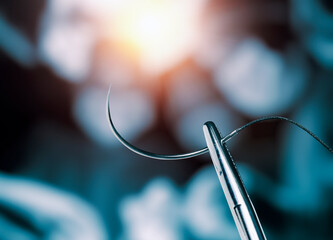 Hemostatic forceps holding half circle cutting needle and suture in front of blurry operators under...