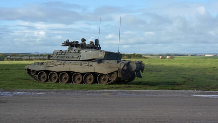Fototapeta premium close-up of Commander and gunner directing a British army FV4034 Challenger 2 ii main battle tank moving across a grass field at speed, on a military exercise, Wiltshire UK