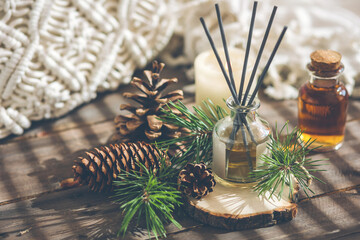 Assortment of natural Christmas essential oils in small bottles. Candles, branches of fir tree, home aroma diffuser. Aromatherapy, cozy atmosphere, holiday festive mood. Close up macro, wooden table