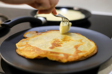 Making bliny at home. Closeup of traditional thin pancakes being buttered with silver fork. Photo with selective focus