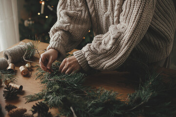 Making Christmas rustic wreath. Hands holding cedar branches, making wreath on wooden table with...