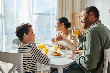 joyful adorable african american boy smiling at his father while his mother looking away, breakfast