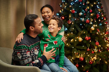 modern cheerful african american family smiling happily at each other with Christmas tree backdrop