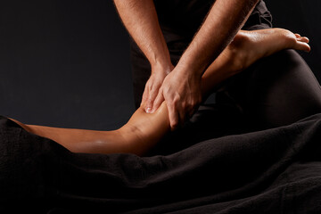handsome male masseur doing a massage on a girl's leg on a black background, concept of therapeutic...