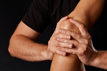 A masseur gives a knee massage to a girl on a dark background, massage of the knee joint - obrazy, fototapety, plakaty