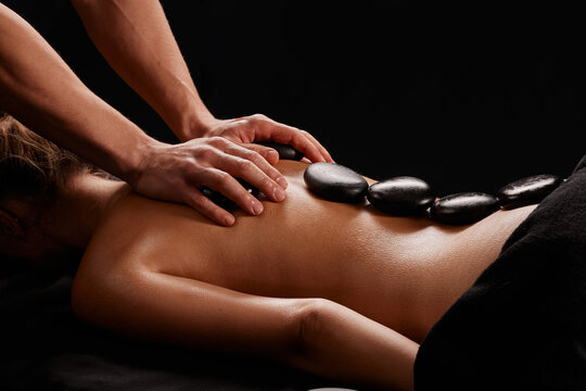 A man receives a hot stone massage, a masseur gives a stone massage