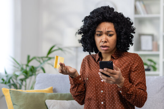 Upset unhappy and cheated woman sitting at home on sofa in living room, displeased rejected online money transfer error, holding bank credit card and phone