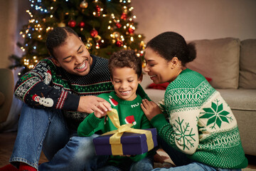 joyous african american family smiling and hugging lovingly next to Christmas tree with garlands