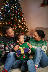 vertical shot of cheerful african american family in cozy sweaters smiling at each other, Christmas