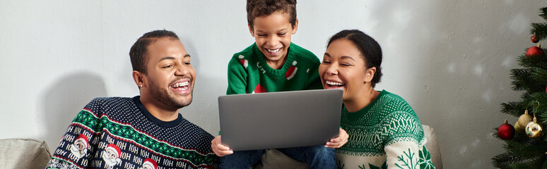 jolly modern african american family sitting on sofa watching movie on laptop, Christmas, banner