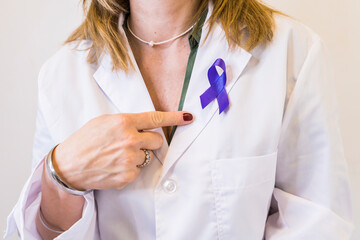 Female doctor wearing a cancer awareness ribbon while pointing at it.