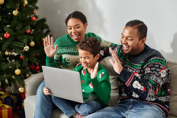 cheerful modern african american family in cozy sweaters waving hi at laptop camera, Christmas