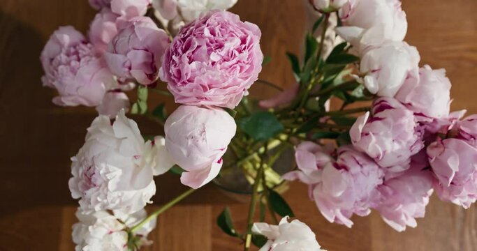 Top view of person puts a bouquet of pink peonies in vase
