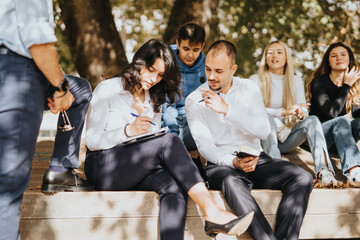 University students gather in a park, studying subjects, solving tasks, and working on a faculty project. They happily exchange knowledge and prepare for exams.